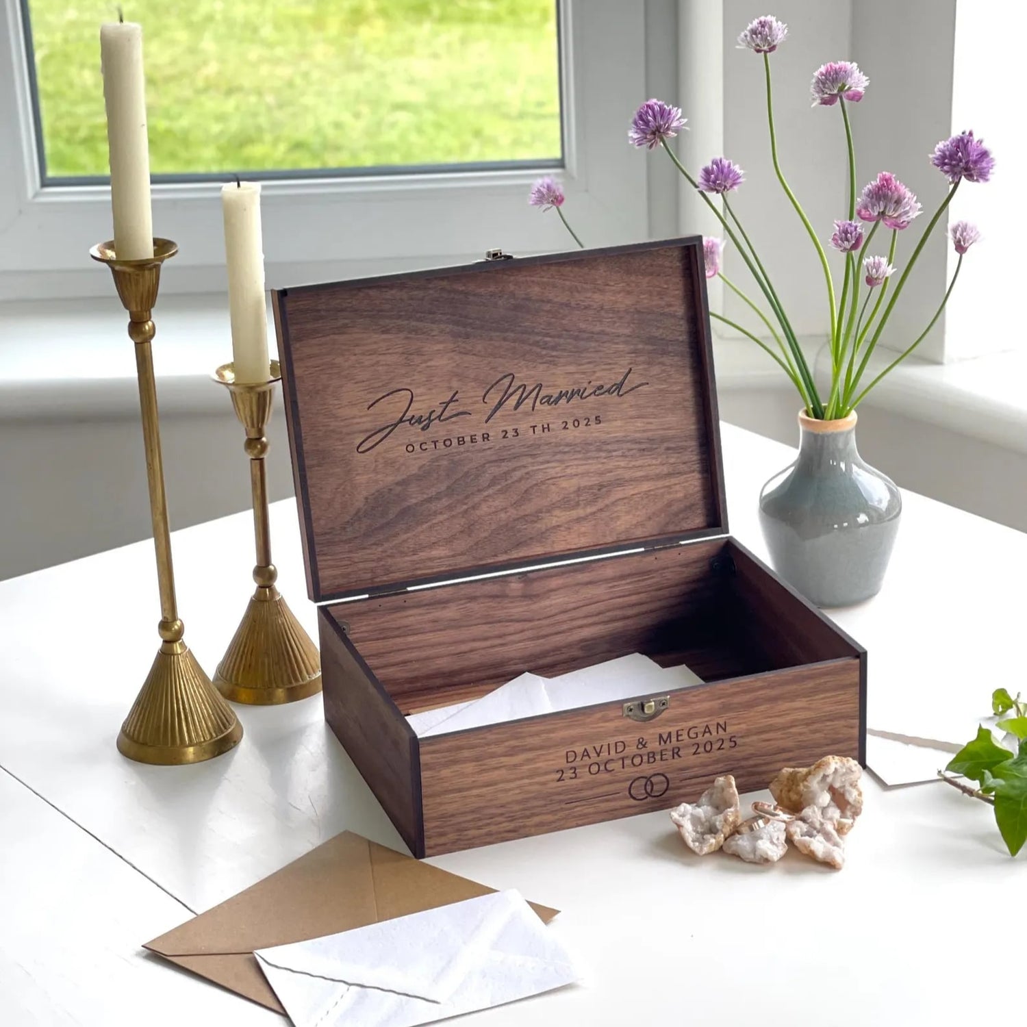 Wooden box engraved with 'Just Married' and personalized details, placed on a table with decorative items.
