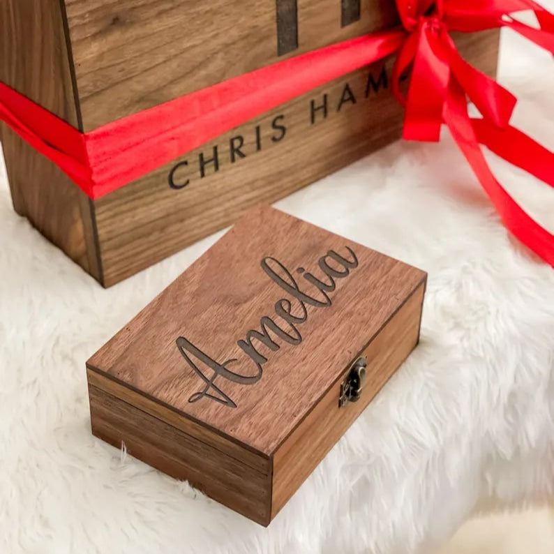 Wooden gift box with red ribbon and engraved name on a white surface
