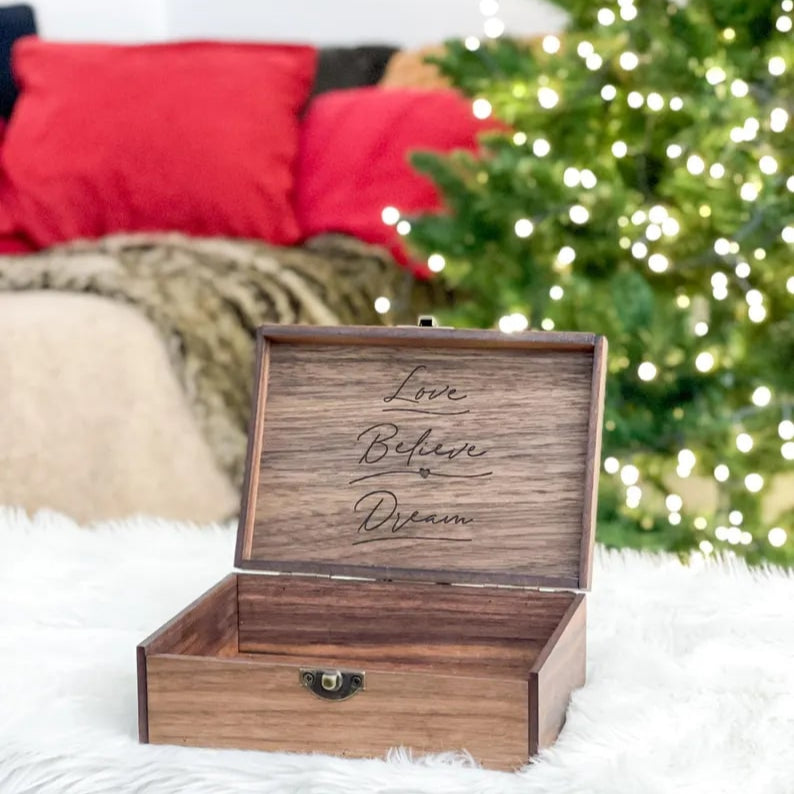 Wooden box with engraved text on a white surface with a Christmas tree in the background