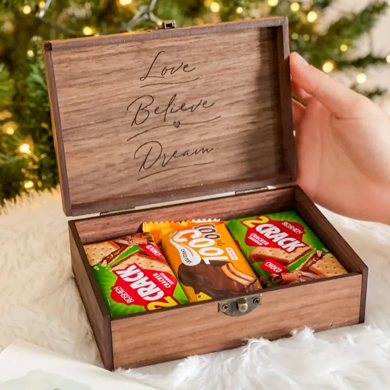 Wooden box with candies inside, held by a hand with a Christmas tree in the background