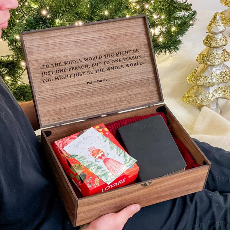 Person holding a wooden gift box with an engraved message, Christmas tree in the background