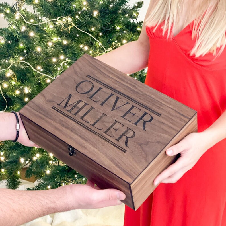 Wooden box with 'Oliver Miller' engraving held by two people in front of a decorated Christmas tree.