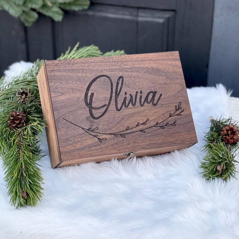 Wooden box with 'Olivia' engraving surrounded by Christmas decorations on a white surface.
