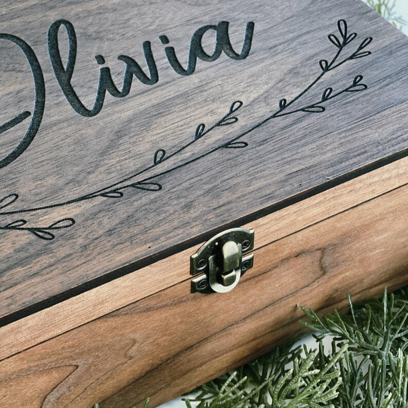 Wooden box with 'Olivia' engraved on it, placed on green grass.