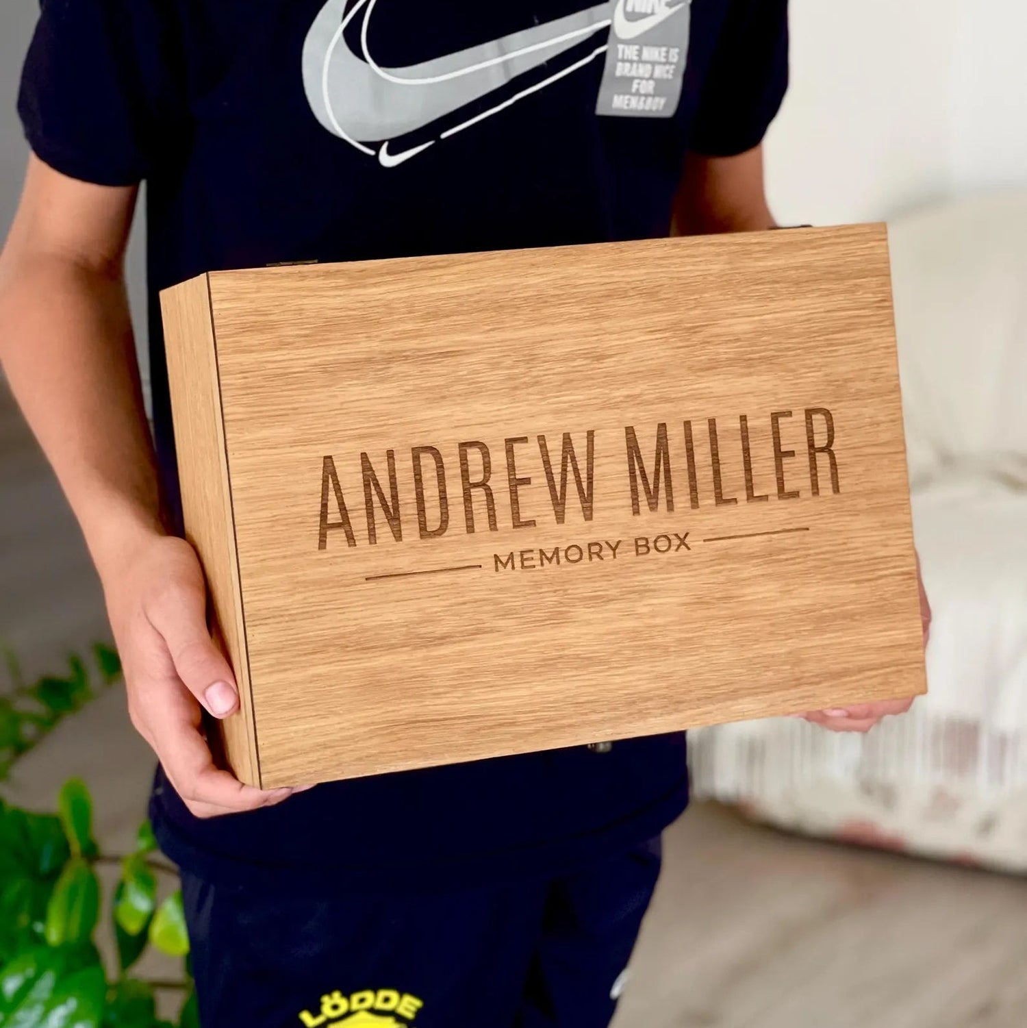 Person holding a wooden box labeled 'Andrew Miller Memory Box' with a Nike logo in the background.