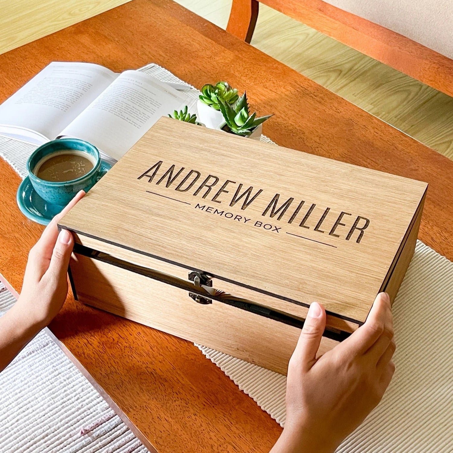 Wooden memory box with 'Andrew Miller' engraved on it, held by hands on a wooden table.
