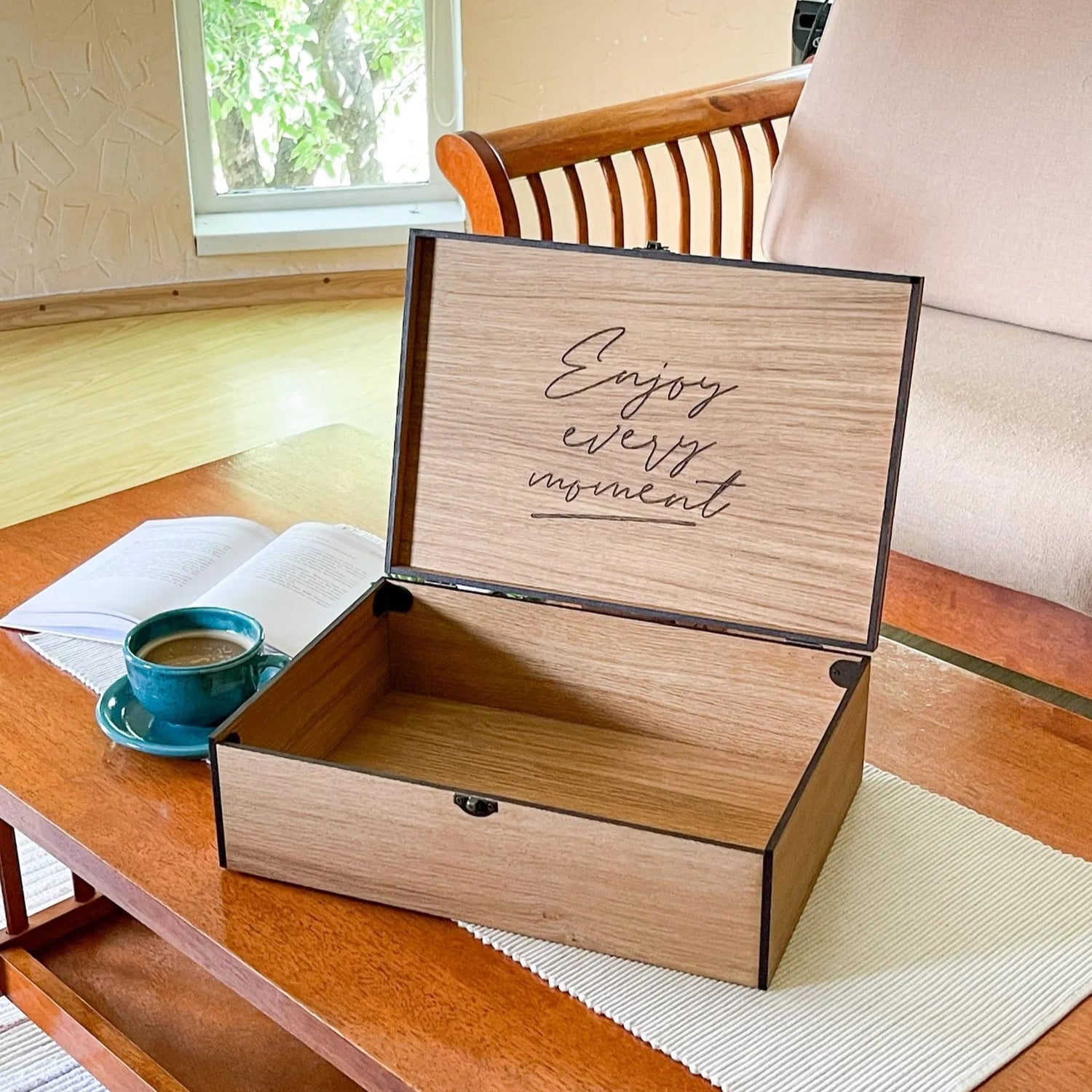 Wooden box with 'Enjoy every moment' text on a wooden table with a cup of coffee.