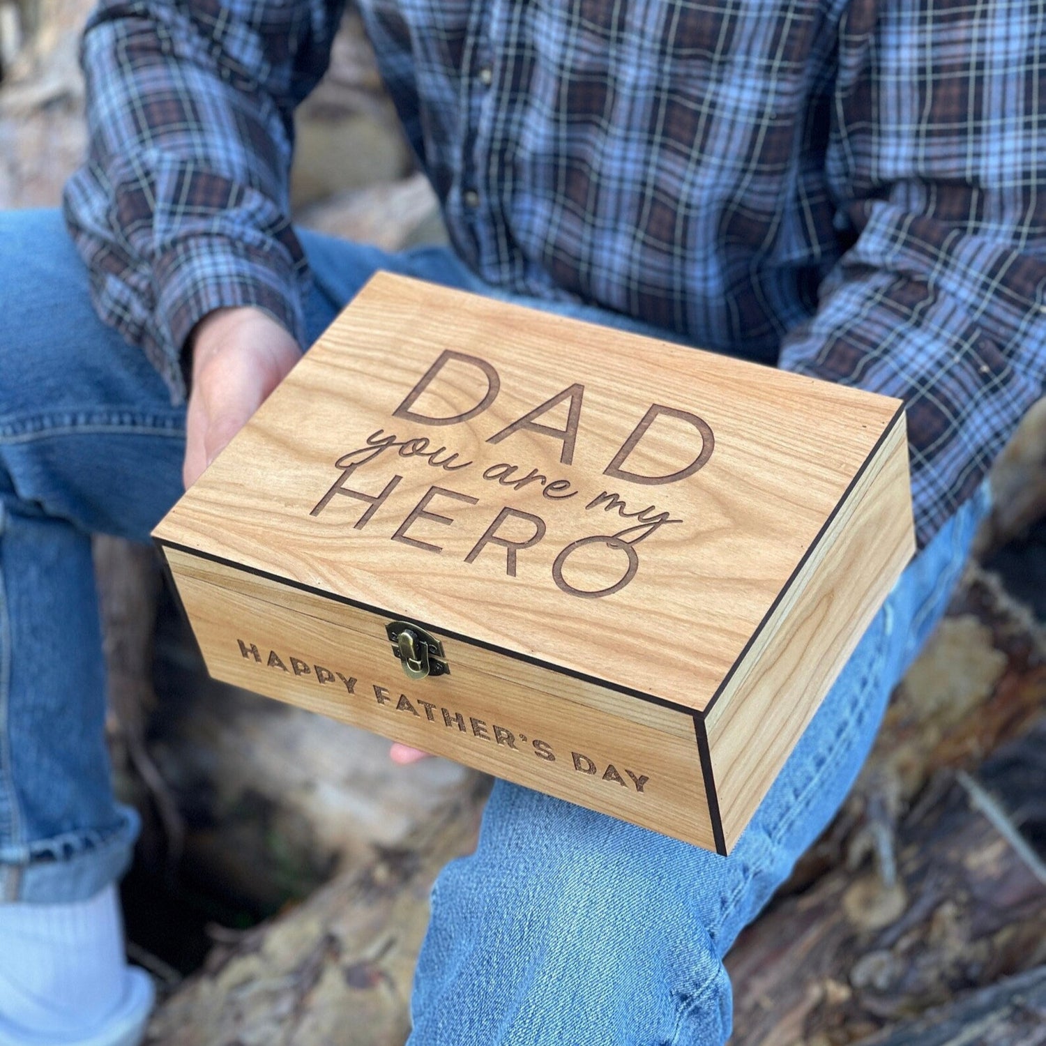 Person holding a wooden box with 'Dad you are my hero' and 'Happy Father's Day' text outdoors.