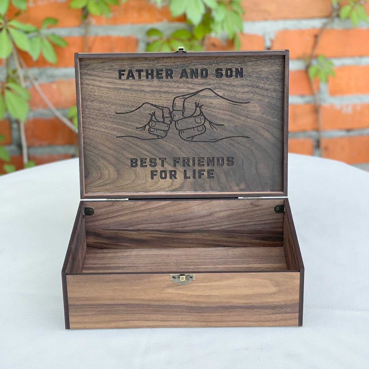 Wooden box with engraved text 'Father and Son Best Friends for Life' against a brick wall background.