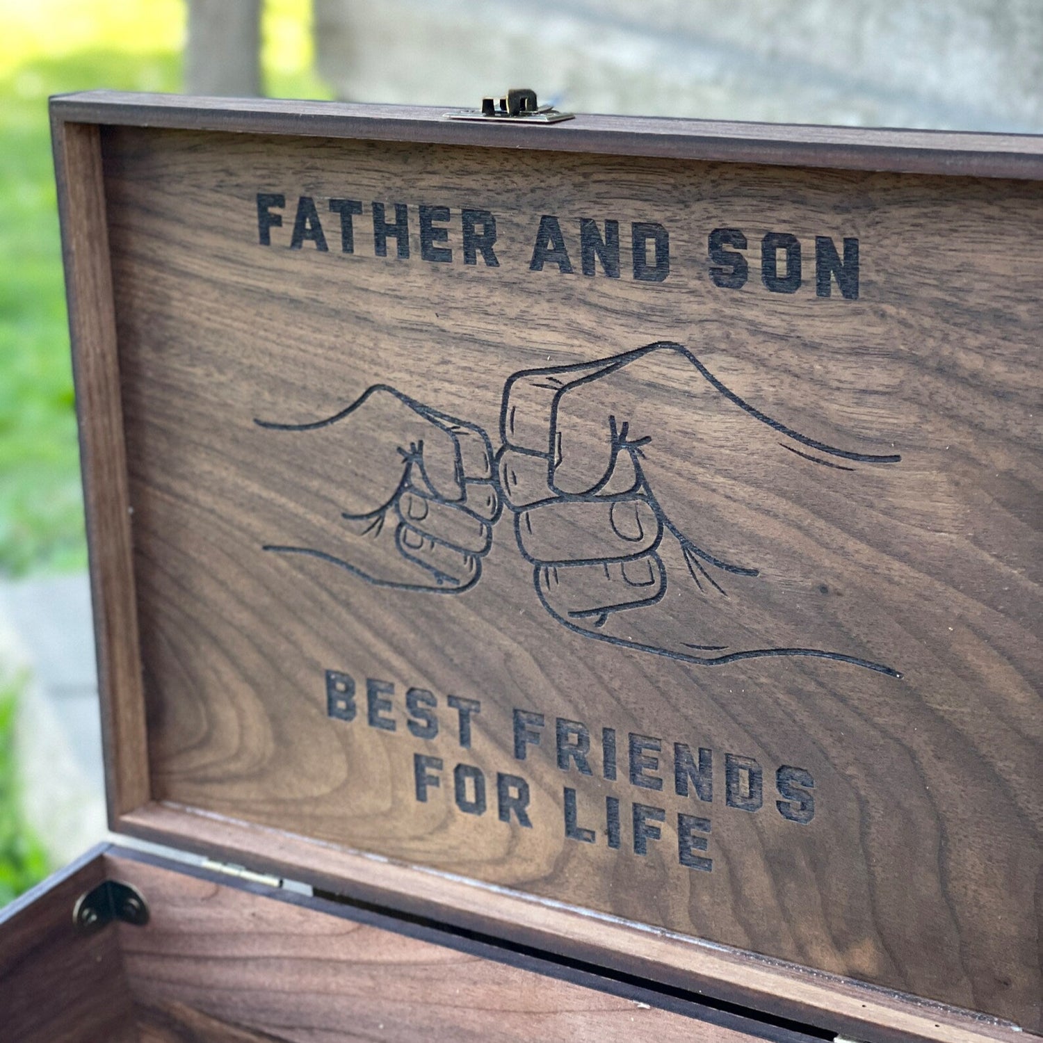 Wooden box with engraved text 'Father and Son Best Friends for Life' on a blurred natural background