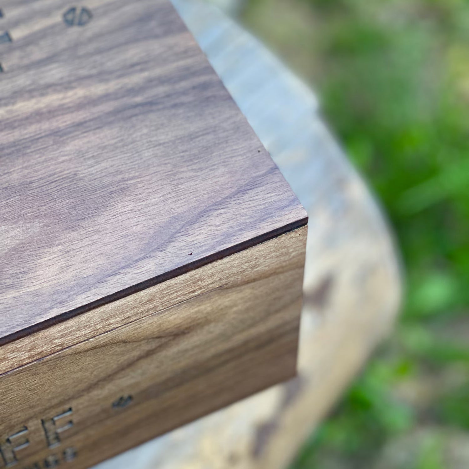Wooden box with 'Bee' engraved on it, placed outdoors with greenery in the background.