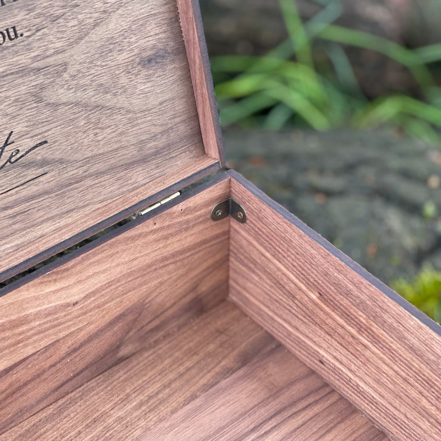 Wooden box with a hinged lid, partially open, on a natural background.