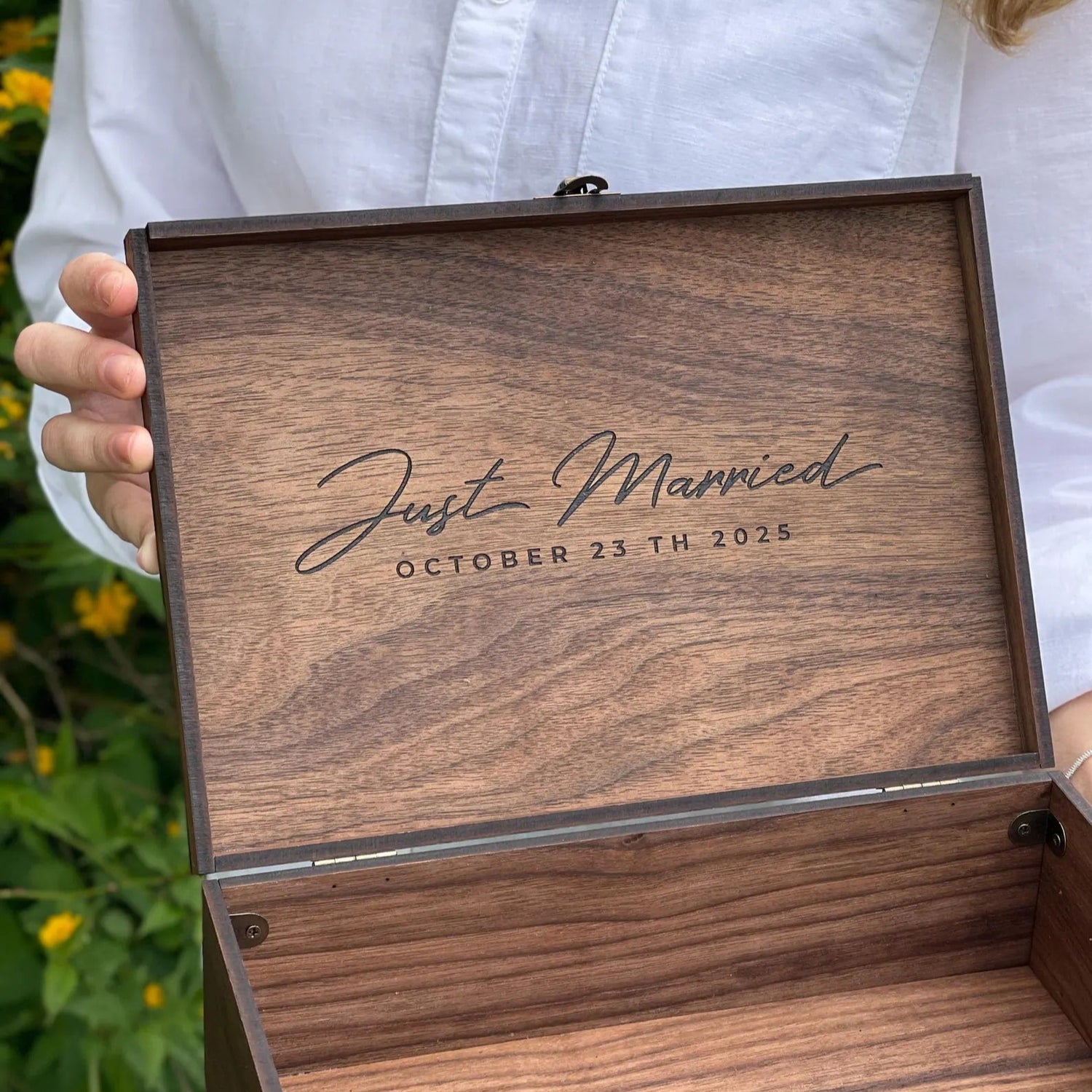Wooden box with 'Just Married' engraving held by a person outdoors.