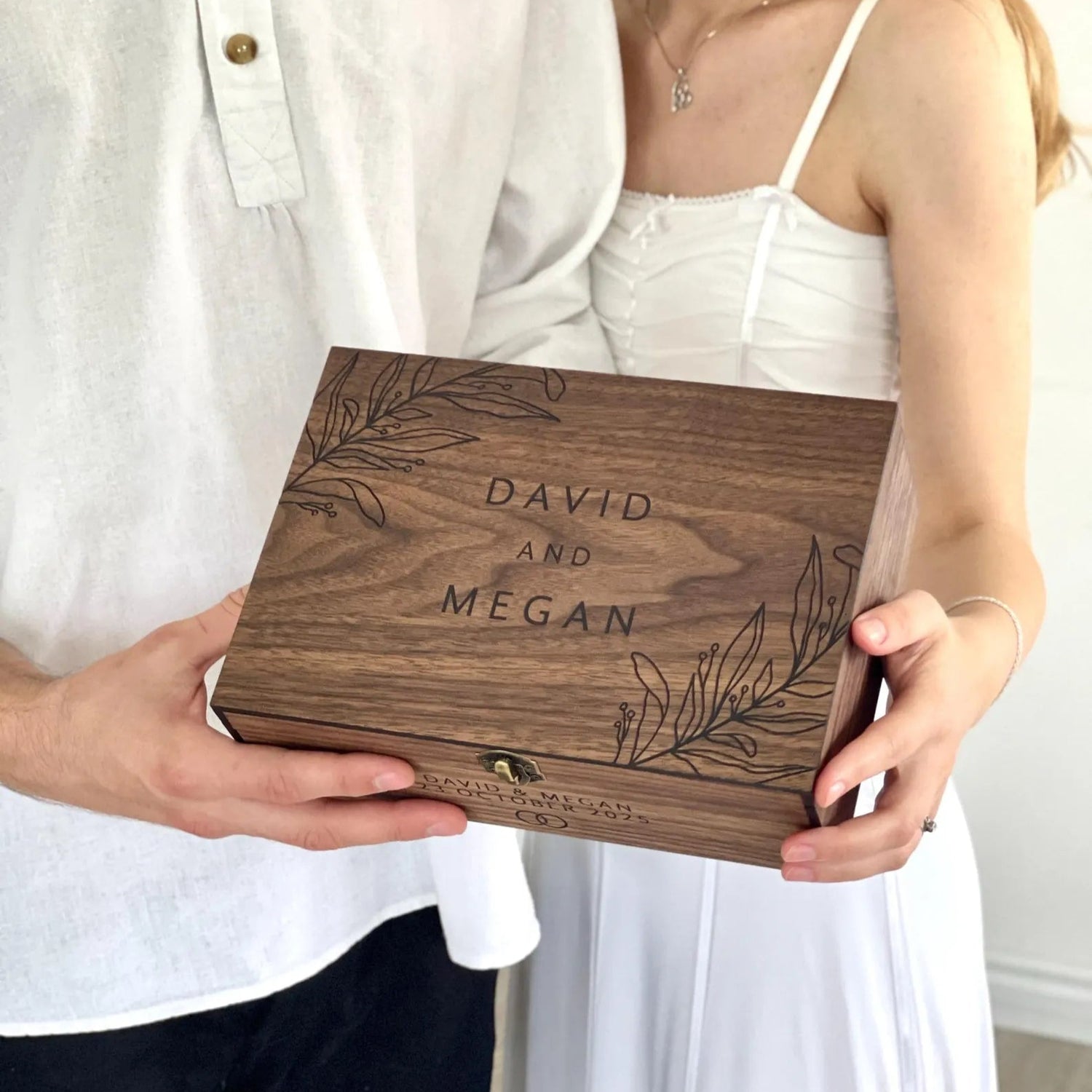 Two people holding a wooden box engraved with 'DAVID AND MEGAN'.