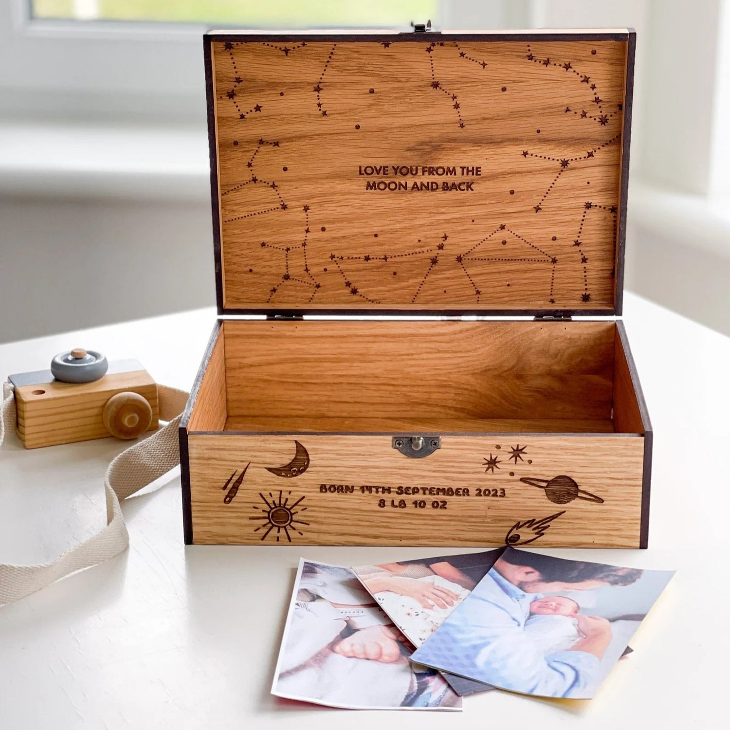 Wooden box with engraved designs and text, placed on a white surface with photos beside it.