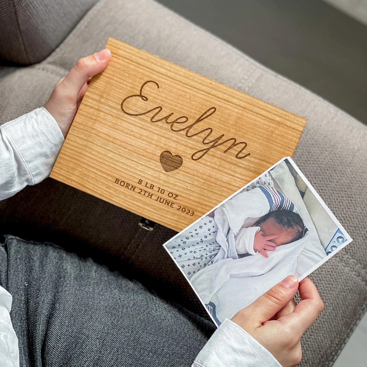 Person holding a wooden box with engraved text and a photo of a baby on a couch.