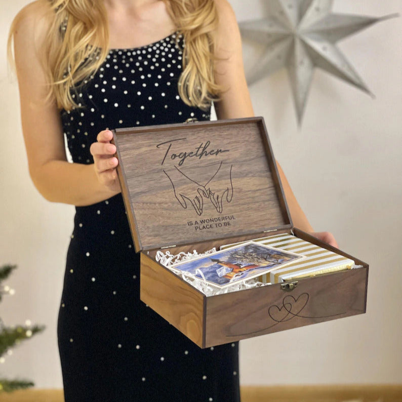 Woman holding a wooden box with engraved design and cards inside, against a neutral background.
