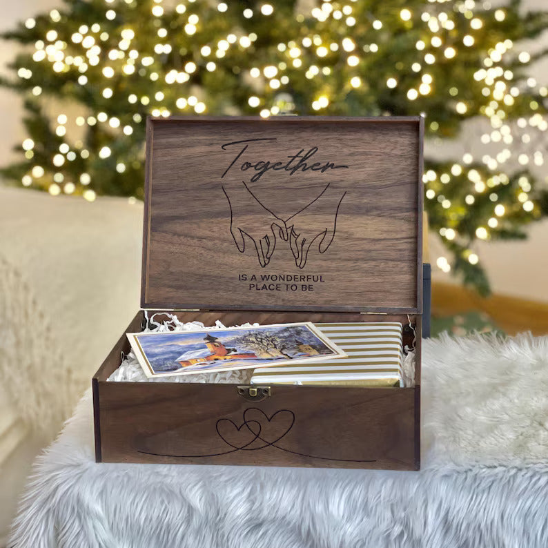Wooden box with engraved design and photos inside, placed on a fluffy surface with a Christmas tree in the background.