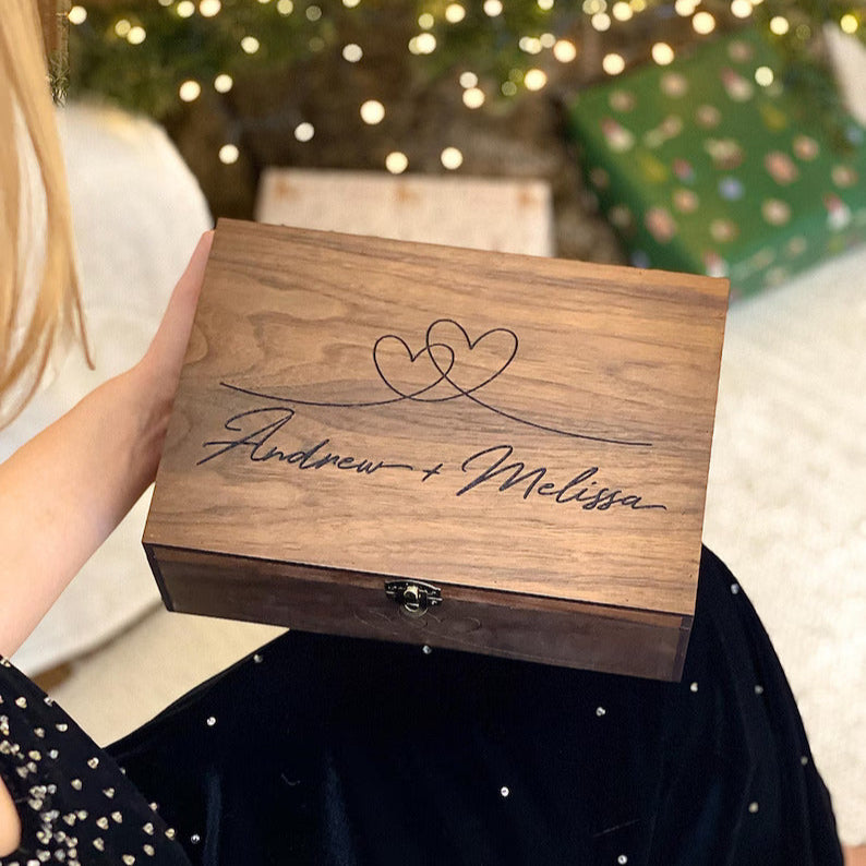 Wooden box with engraved names held by a person in front of a decorated Christmas tree.