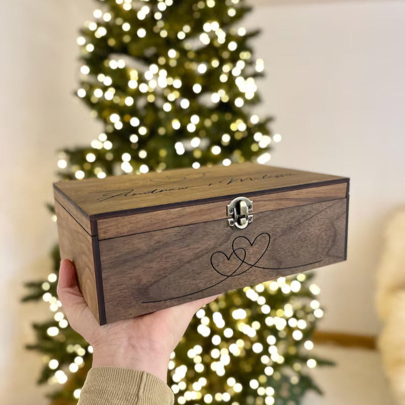 Wooden box with engraved design held in front of a decorated Christmas tree.