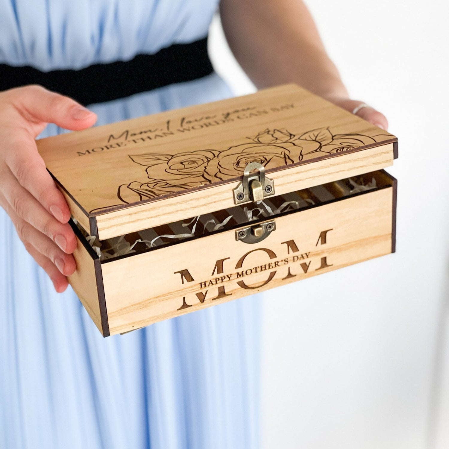 Wooden jewelry box with floral design and 'Mom' engraving held by a person.