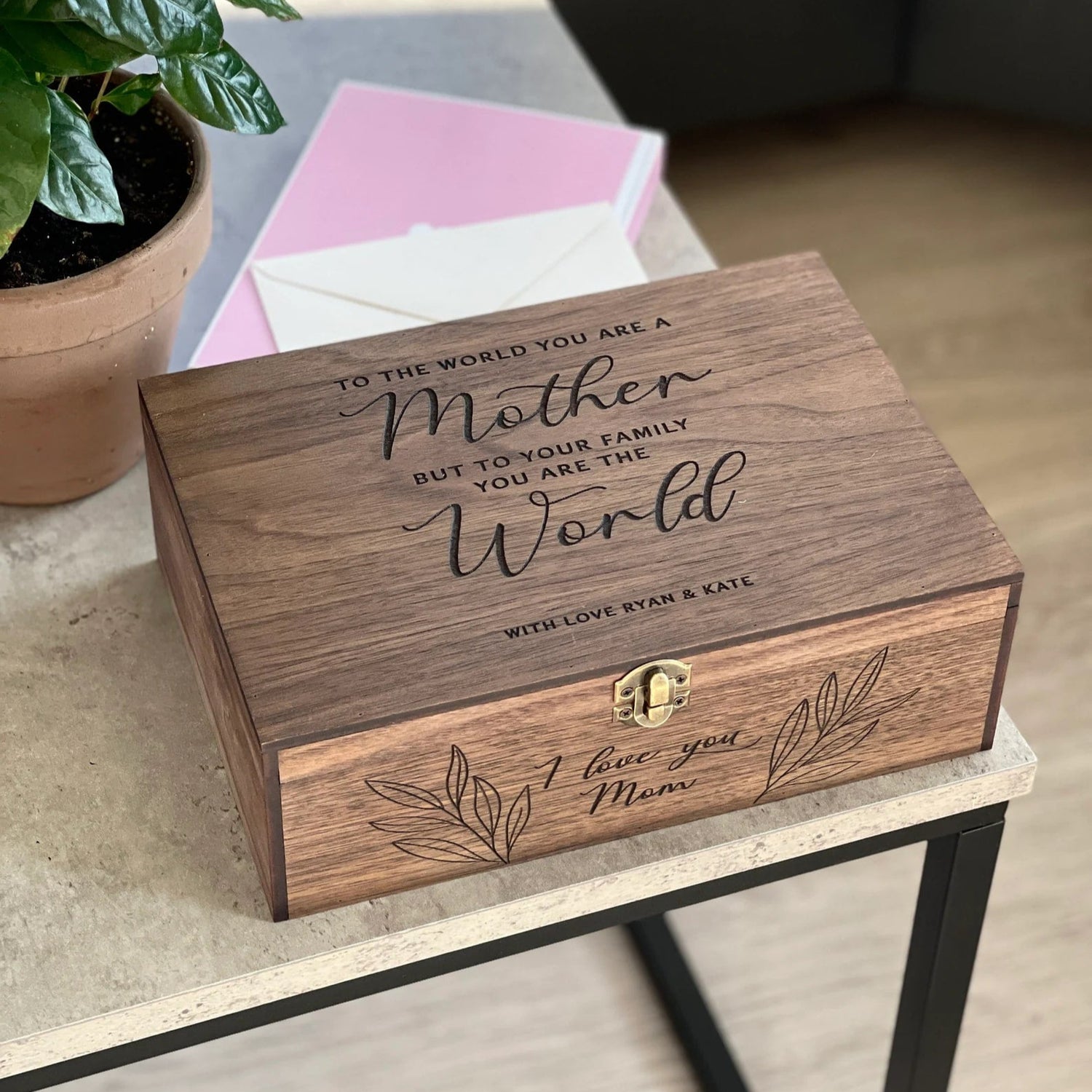 Wooden box with engraved message on a table with a plant and pink card in the background