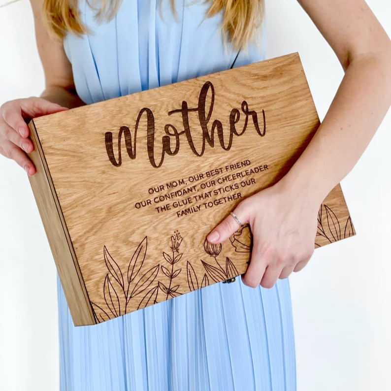 Person holding a wooden box engraved with 'Mother' and text, wearing a light blue dress.