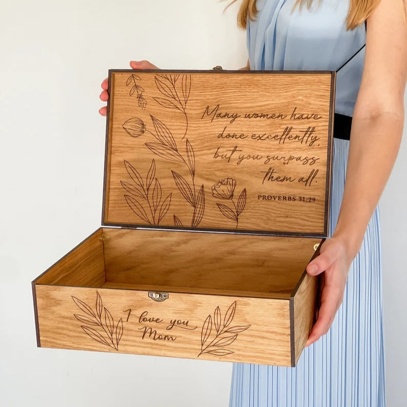 Wooden box with engraved text and floral designs held by a person wearing a light blue dress.