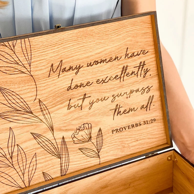 Wooden box with engraved text and floral designs, held by a person.