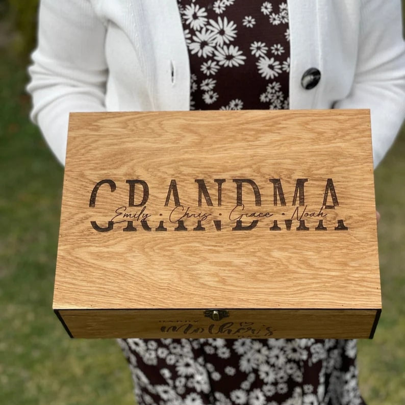 Person holding a wooden box engraved with 'GRANDMA' outdoors