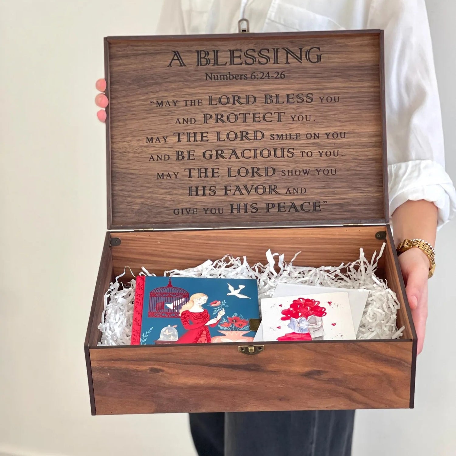 Wooden gift box with engraved message held by a person, containing books inside.