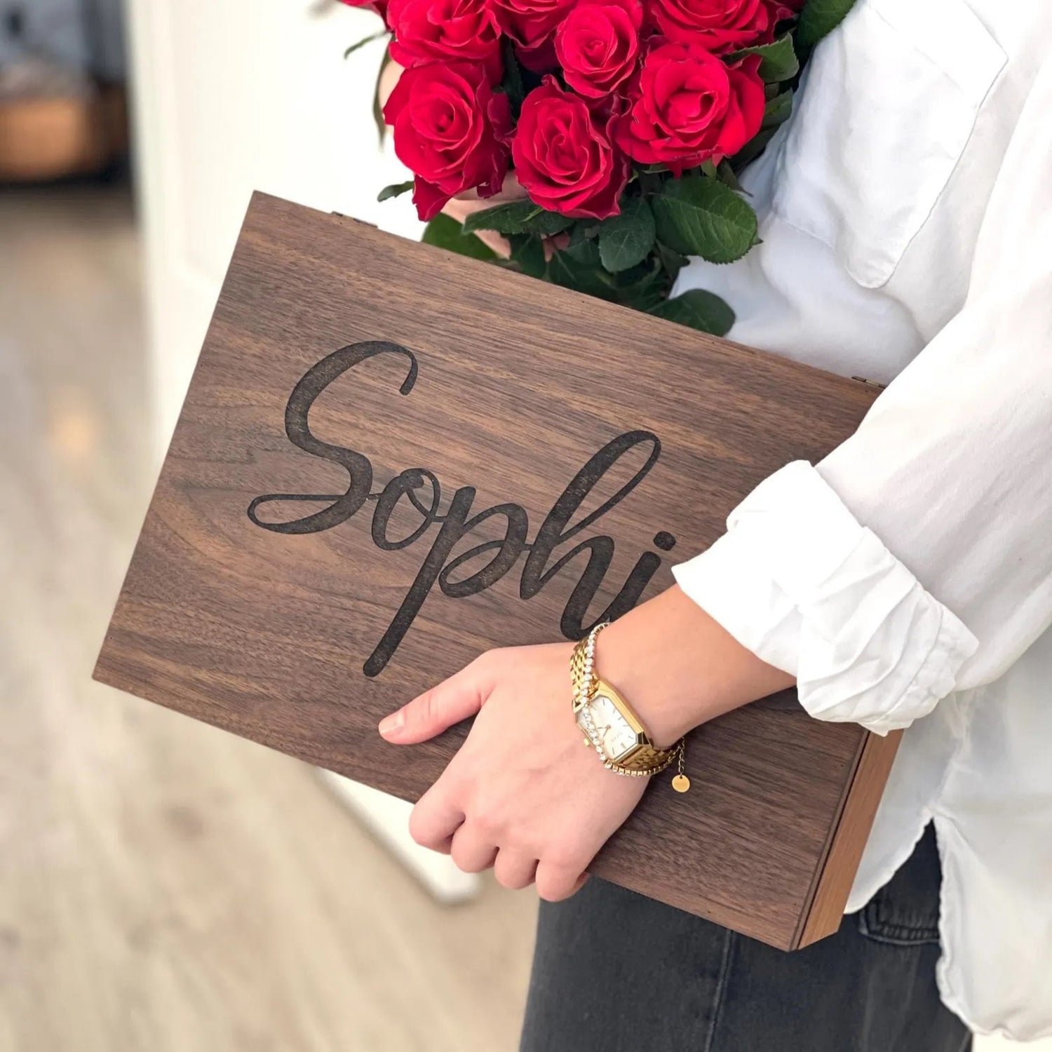 Person holding a bouquet of red roses and a wooden box with 'Sophia' engraved.