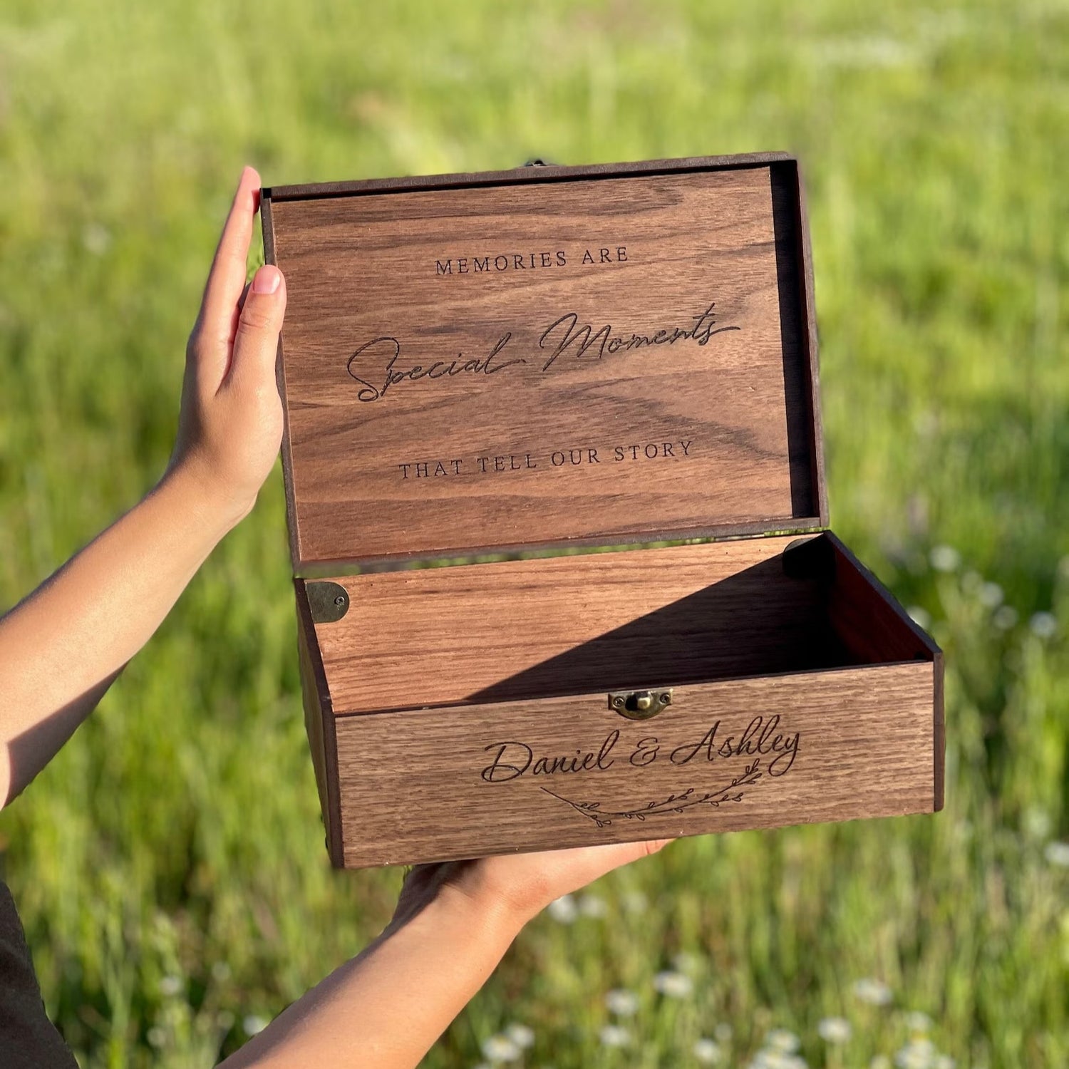 Wooden box with engraved text held in a hand against a grassy background