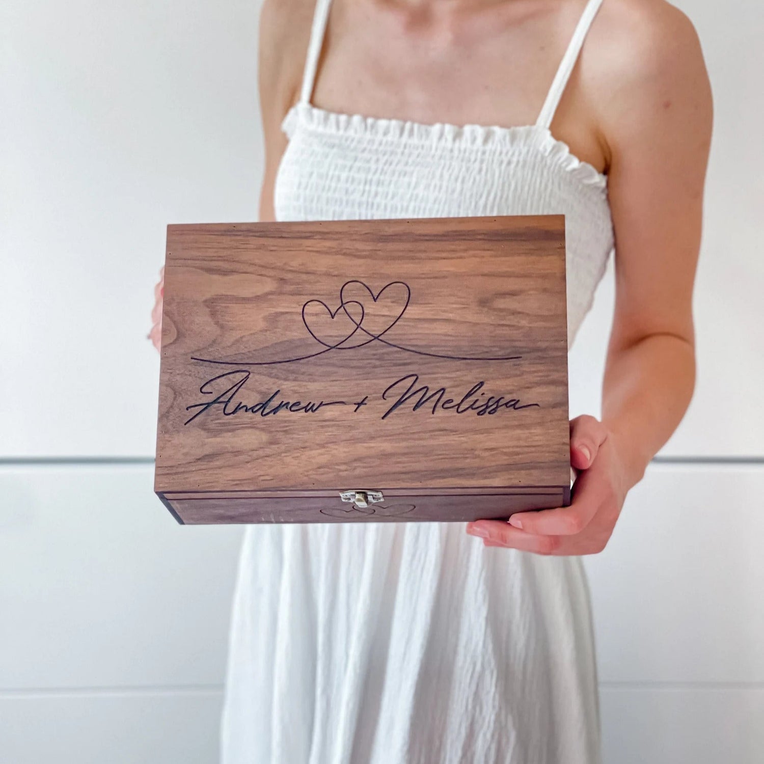 Person holding a wooden box with engraved names against a white background