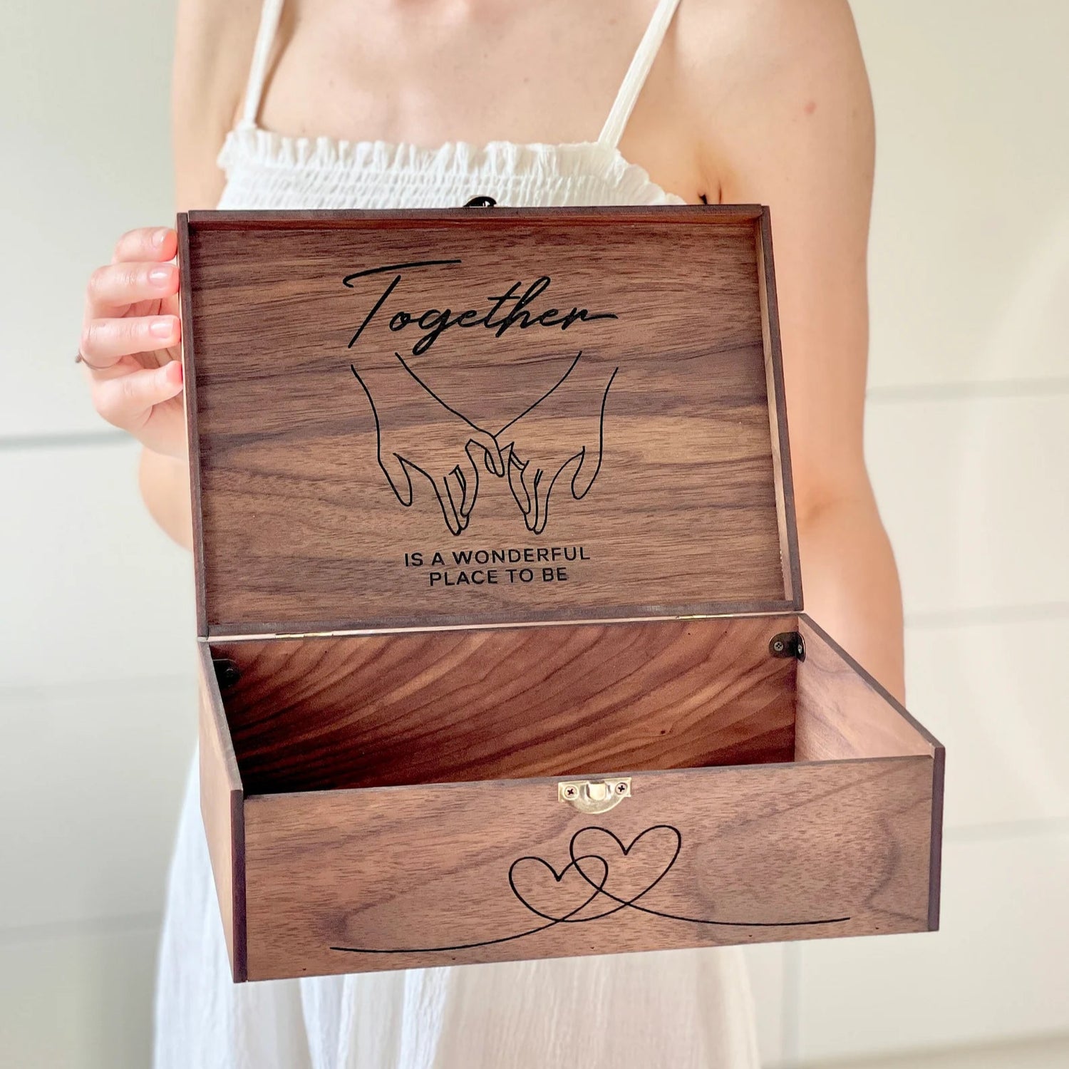 Wooden box with engraved text held by a person wearing a white dress.