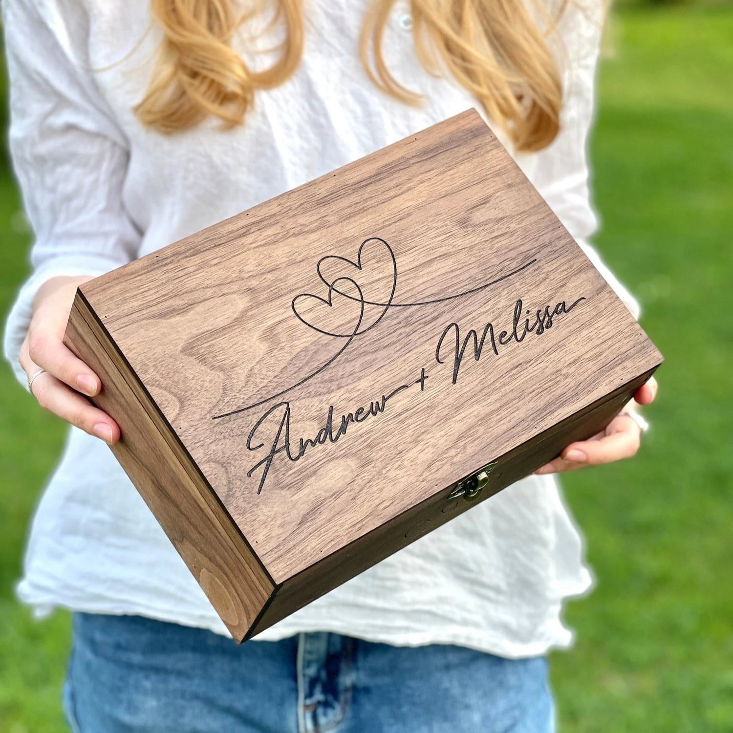 Person holding a wooden box with engraved names outdoors