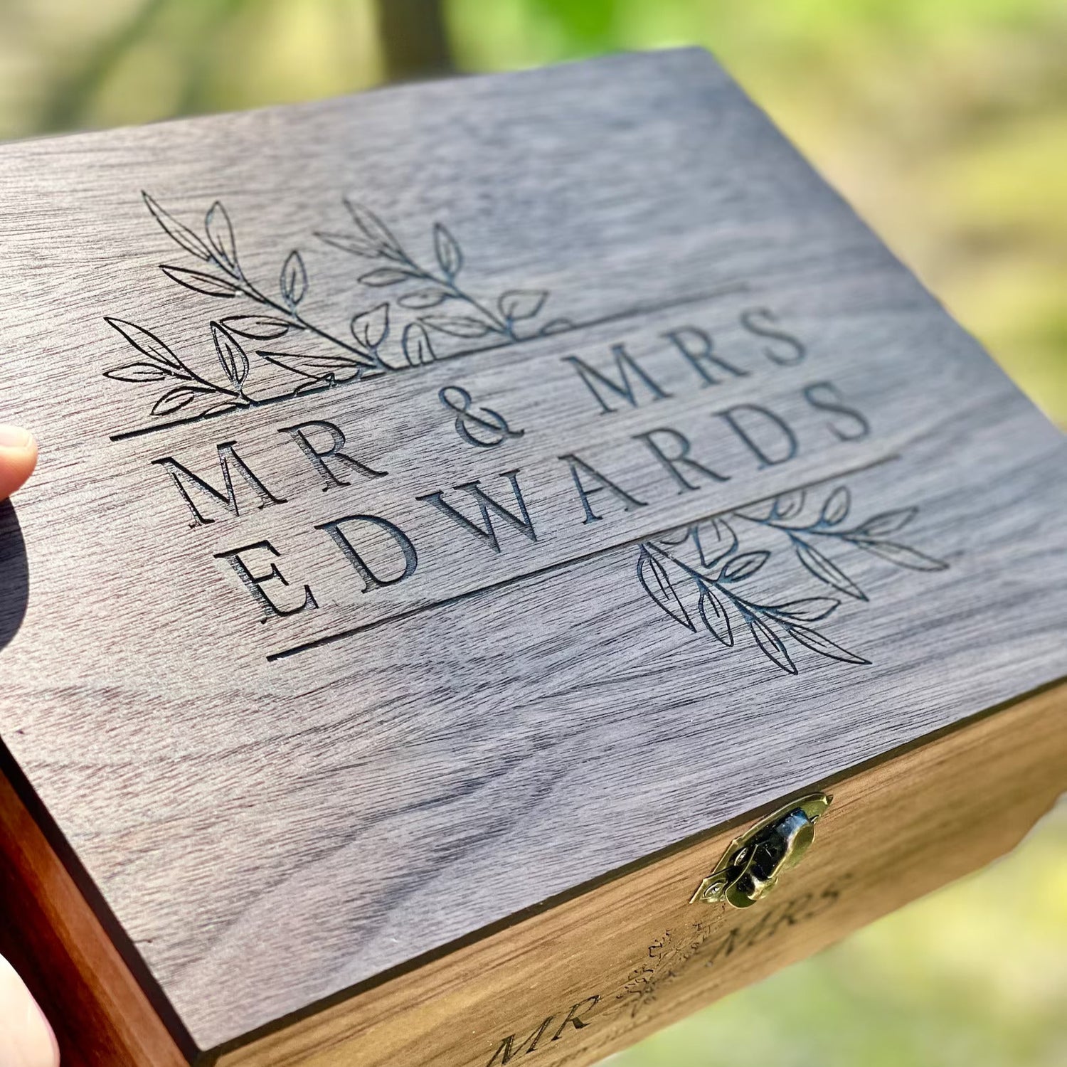 Wooden box with 'MR & MRS EDWARDS' engraving against a blurred natural background