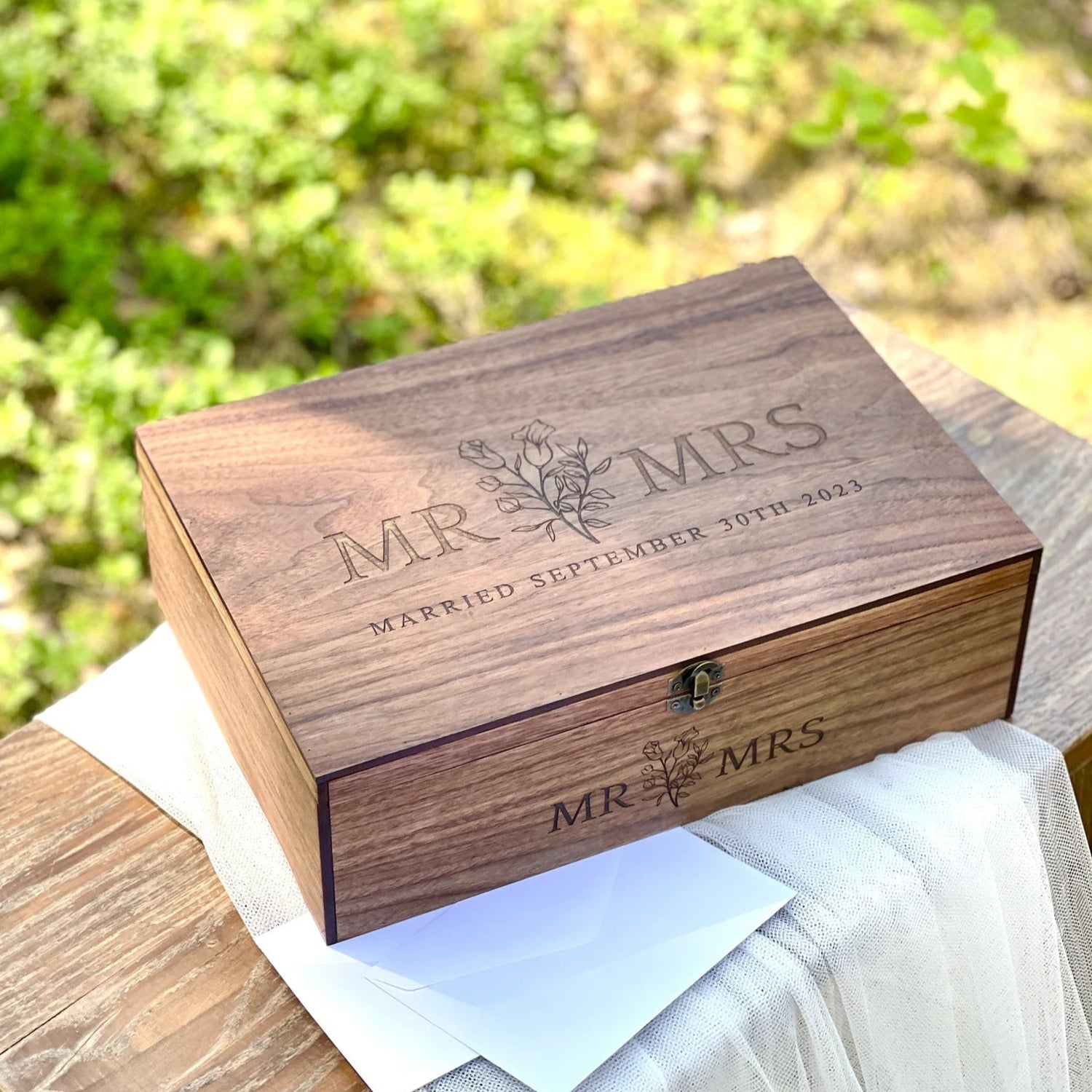 Wooden box engraved with 'MR & MRS' on a wooden surface with a blurred natural background.