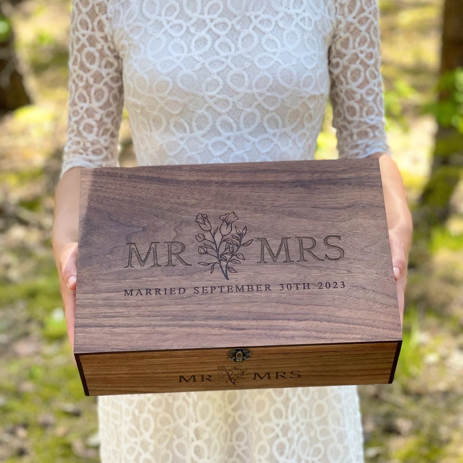Person holding a wooden box engraved with 'MR & MRS' and a date, outdoors.