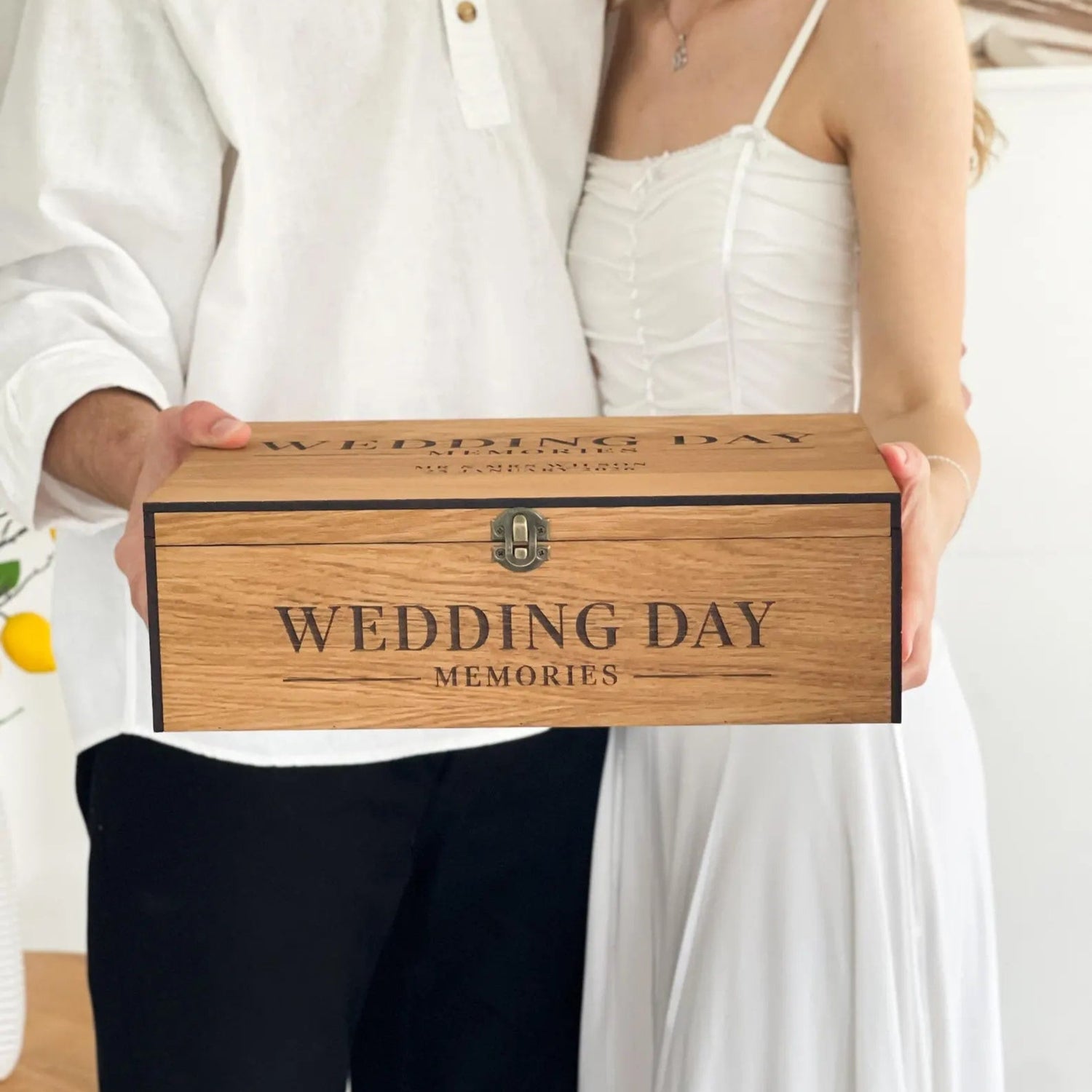 Couple holding a wooden box labeled 'Wedding Day Memories' in an indoor setting.