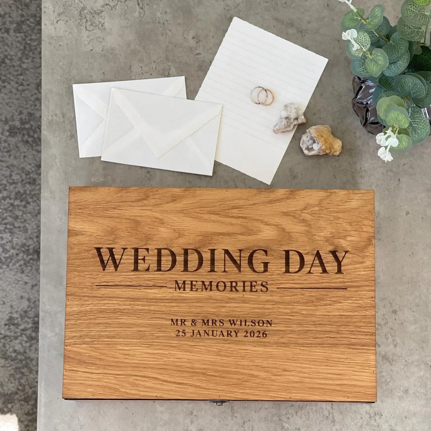 Wooden box labeled 'Wedding Day Memories' with envelopes on a concrete surface.