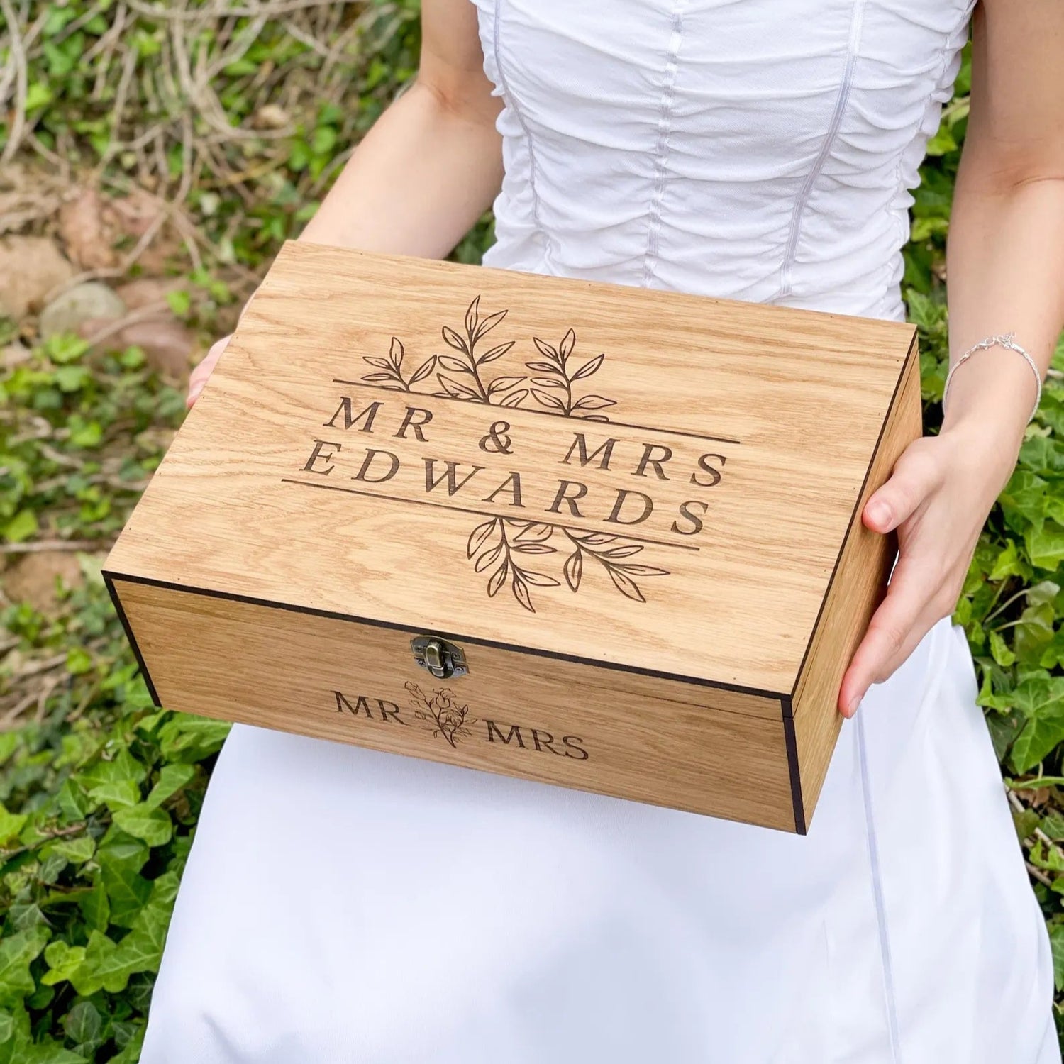 Person holding a wooden box engraved with 'MR & MRS EDWARDS' against a natural background.