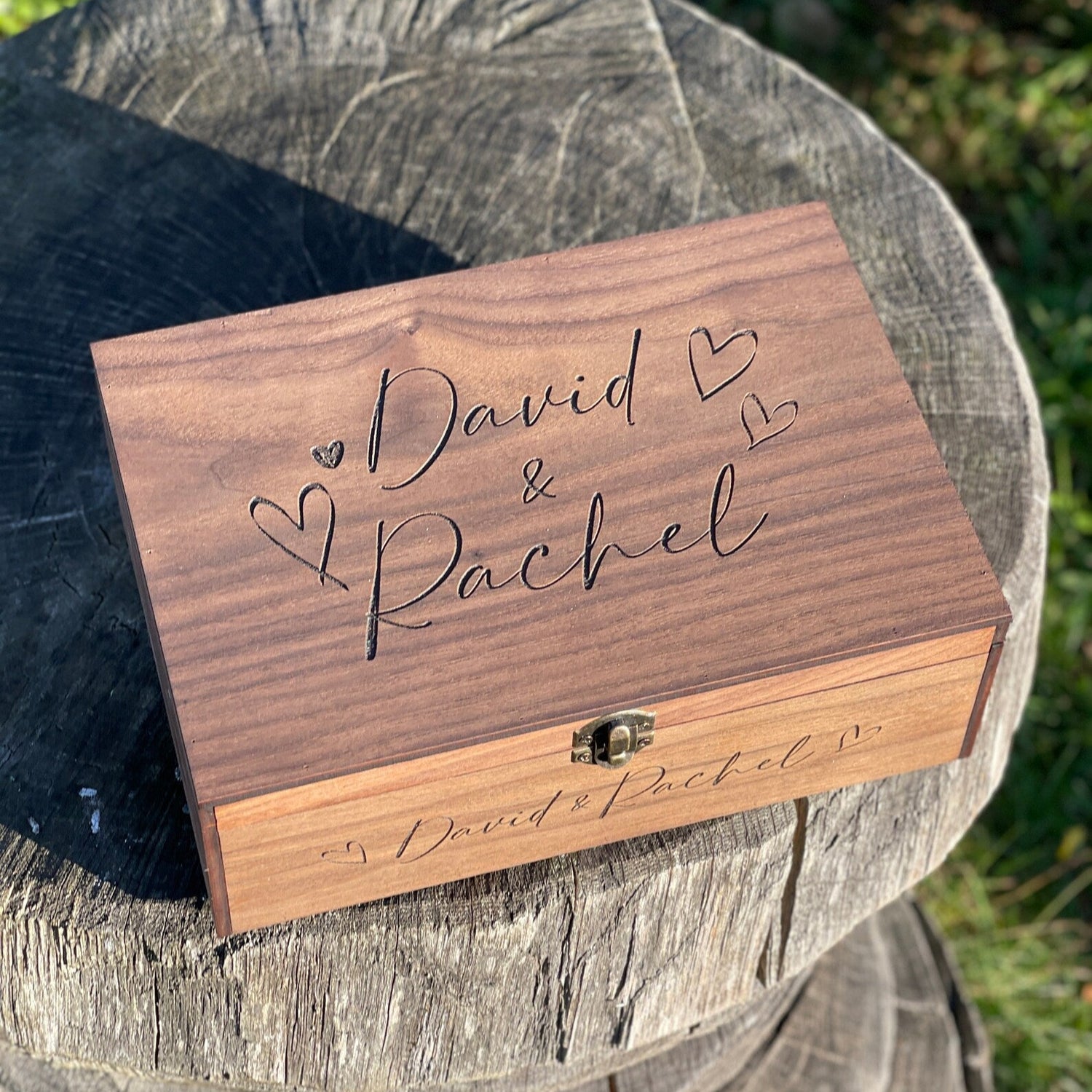 Wooden box engraved with 'David & Rachel' on a wooden surface outdoors.