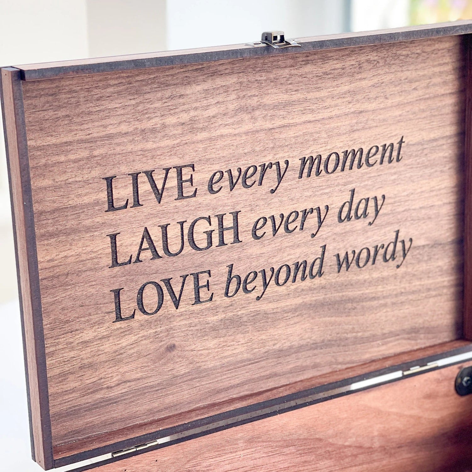 Wooden box with engraved text 'LIVE every moment LAUGH every day LOVE beyond wordy' on a light background.