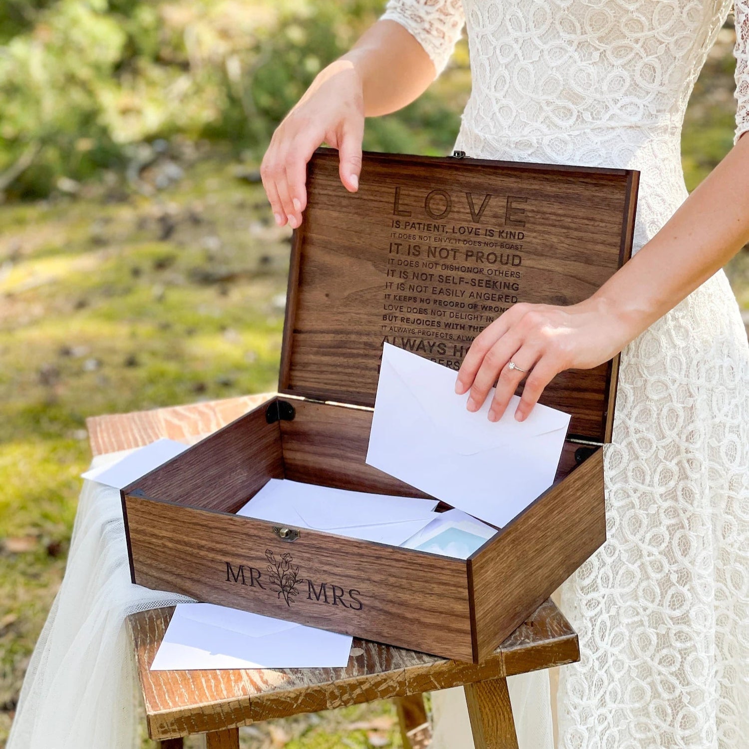 Wooden box with engraved text held by a person in a white dress outdoors.