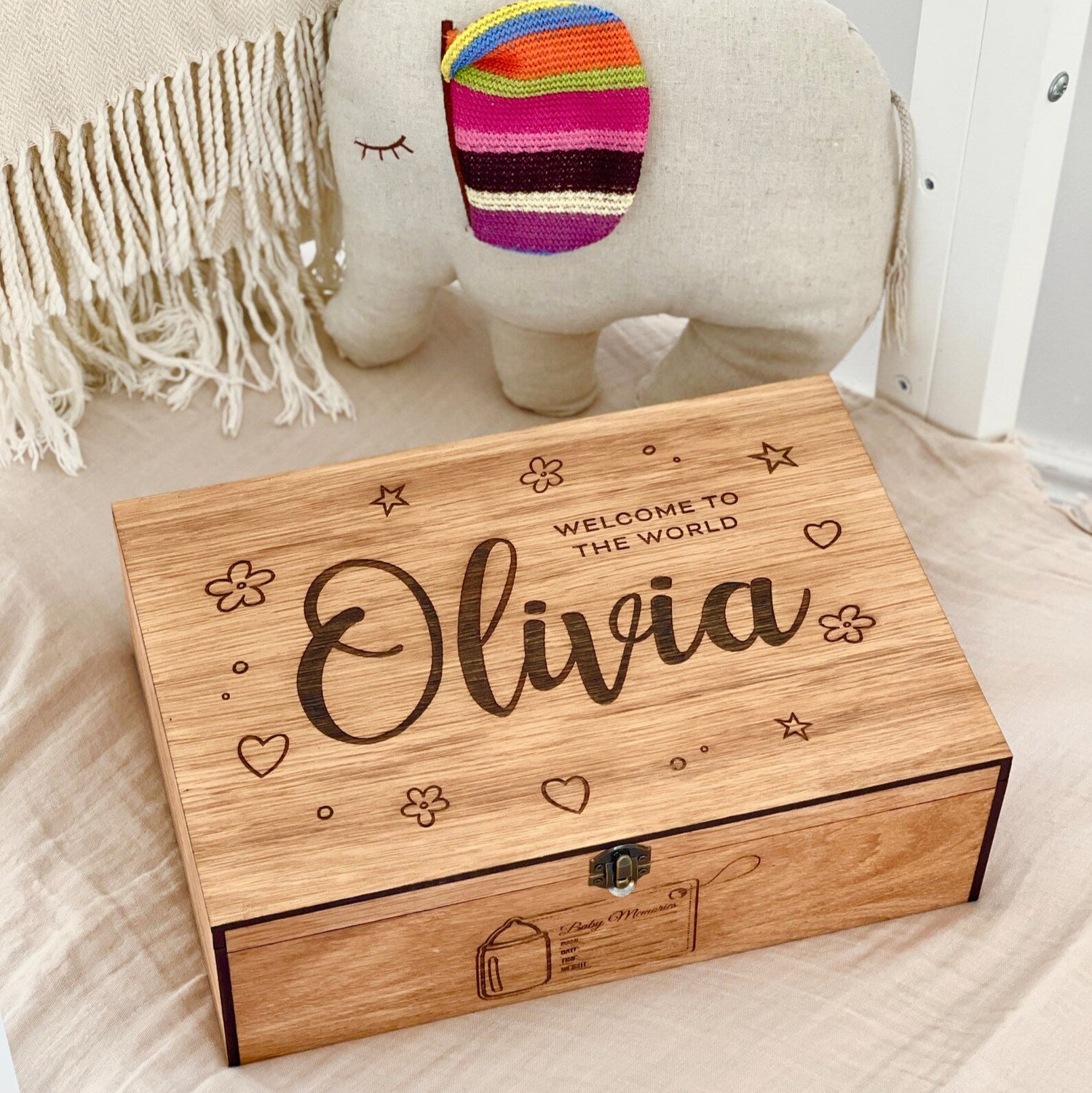 Wooden box with engraved text 'Welcome to the World Olivia' on a soft surface.