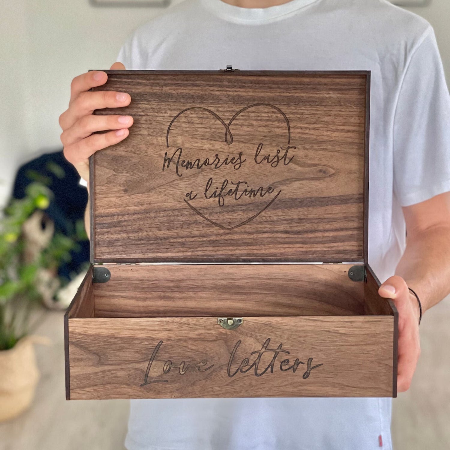 Person holding a wooden box with engraved text, standing indoors.