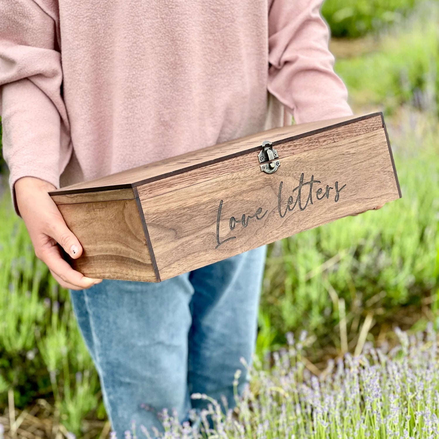 Person holding a wooden box engraved with 'Love letters' in a lavender field