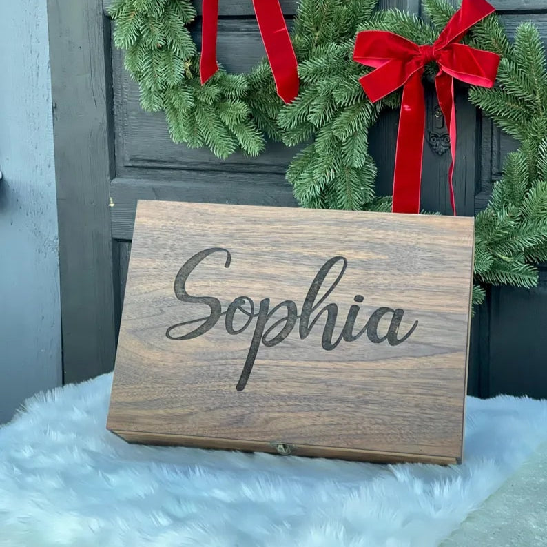 Wooden sign with 'Sophia' engraved, in front of Christmas wreaths with red bows on a door.
