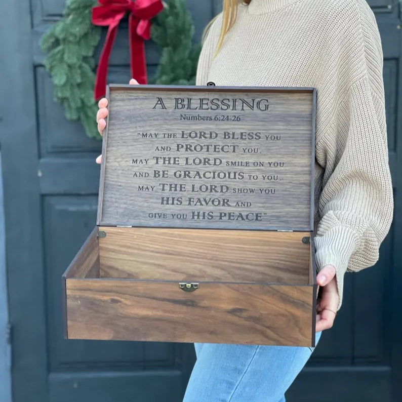 Person holding a wooden box with engraved text in front of a door with a wreath.